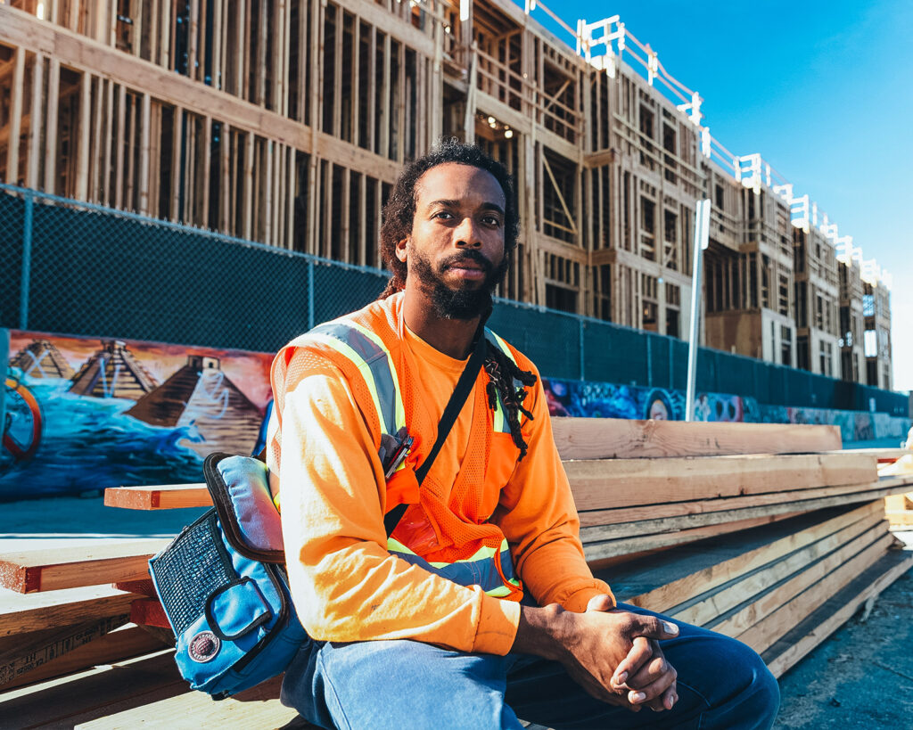 Man wearing a reflector vest sits in front of a new housing development project.