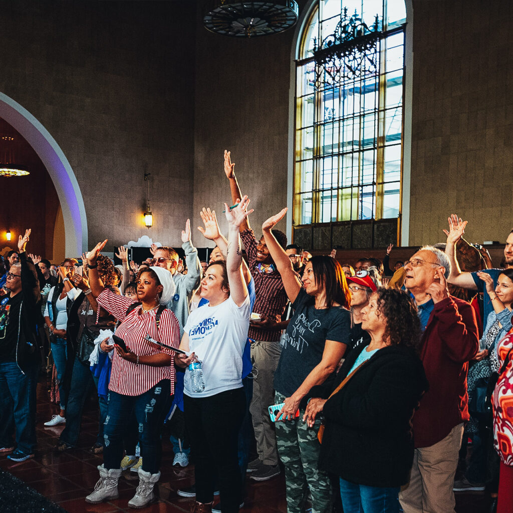 A crowd of people smile and raise their hands.