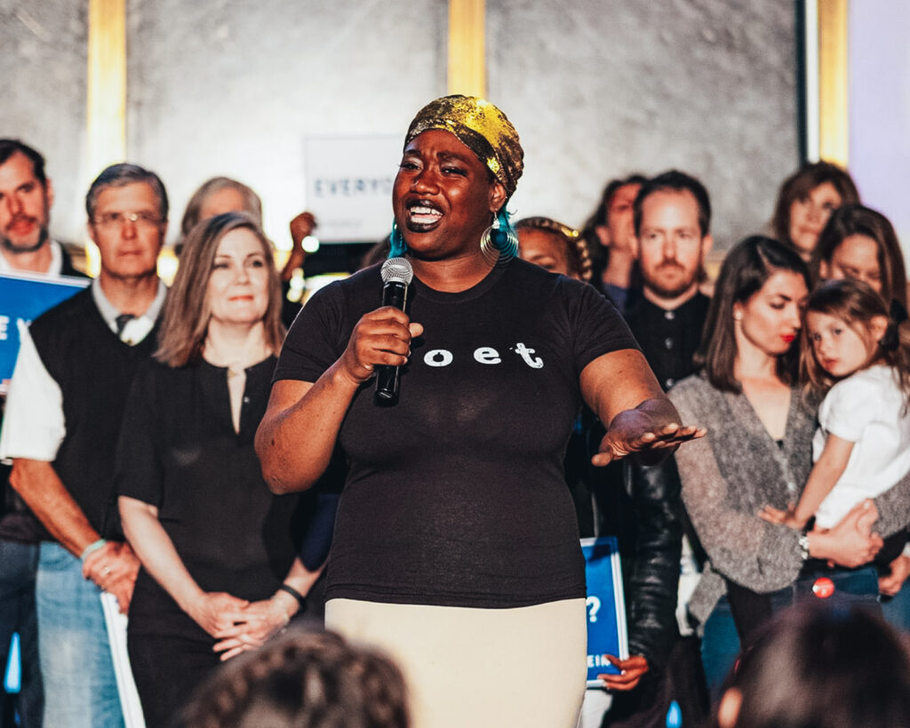 Woman wearing "poet" t-shirt engages her audience with energy