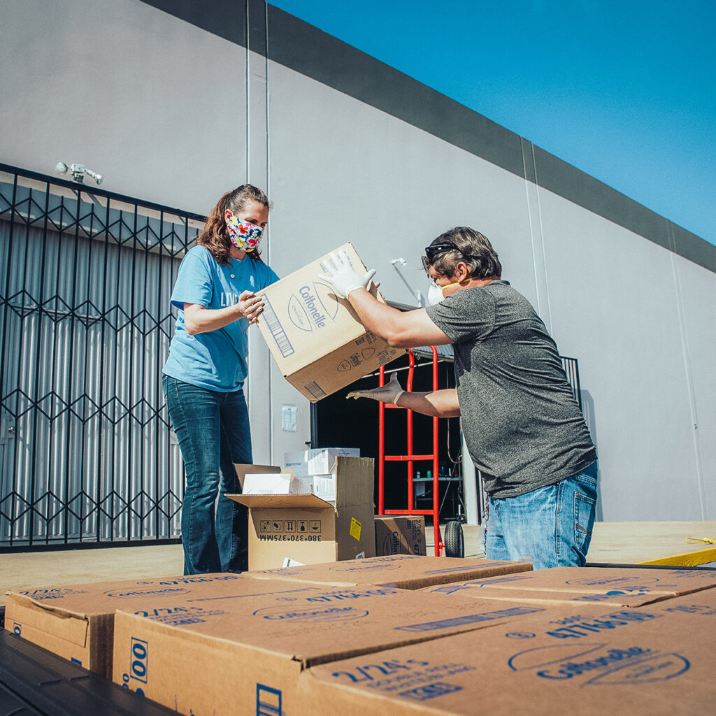 Two volunteers in masks load boxes of paper products for distribution to those in need