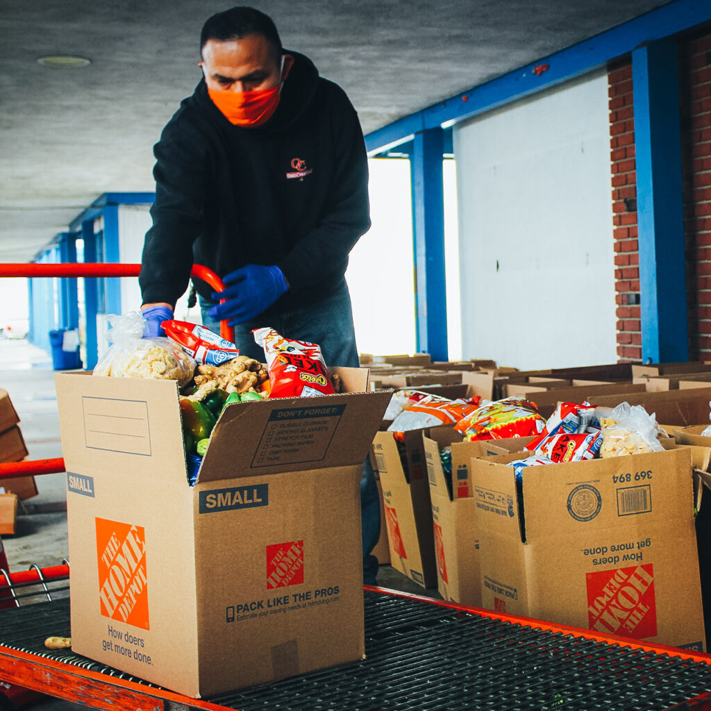 A man wearing a mask helps load food drive items into cardboard boxes